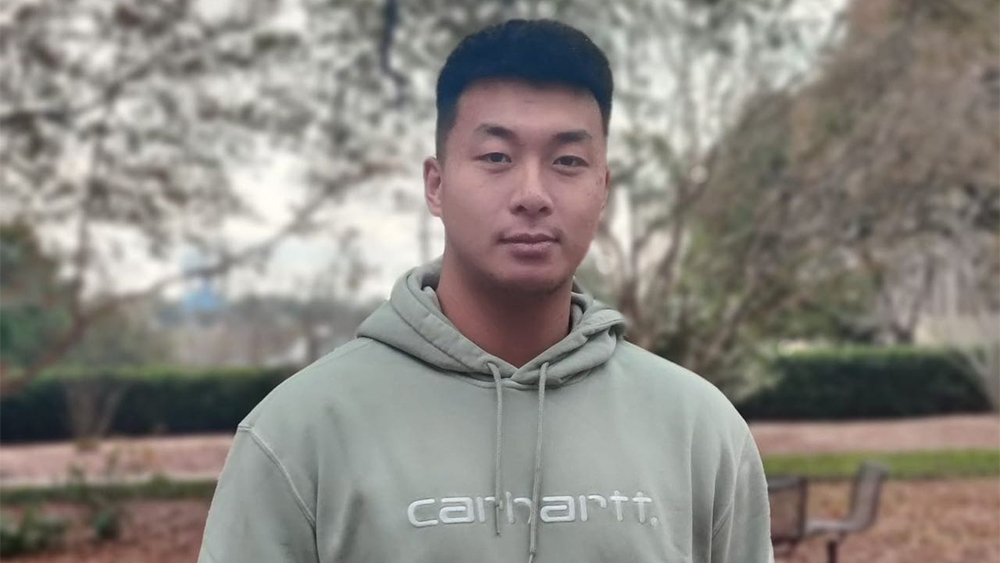 Justin, an international student from China who earned his master's degree in sport and entertainment management from the University of South Carolina, stands in front of a tree on the University of South Carolina campus