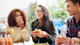Two women and one man go out for American Food, eating burgers, sitting at a table, with one covering her mouth as she laughs. In American culture food brings many students together in social situations.
