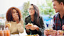 Two women and one man go out for American Food, eating burgers, sitting at a table, with one covering her mouth as she laughs. In American culture food brings many students together in social situations.