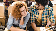 A man and and woman sitting next to each other compare notes in a busy lecture hall.
