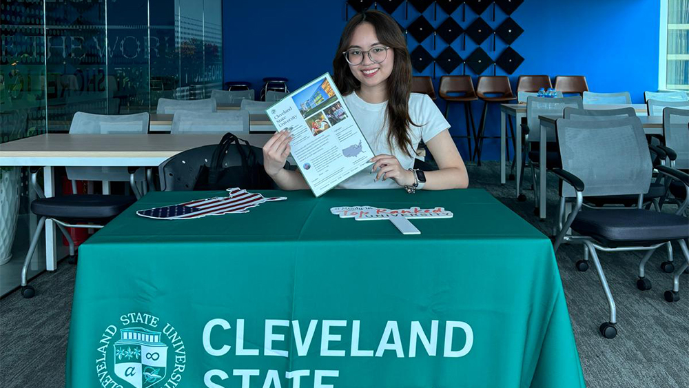 Kate, a Cleveland State Global student ambassador from Vietnam, sits at a table at a university fair and holds up a Cleveland State Global brochure