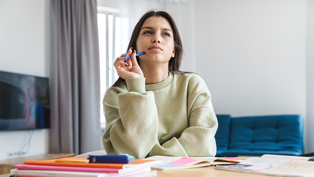 Woman holding a pen and looking thoughtfully to the side in a bright workspace