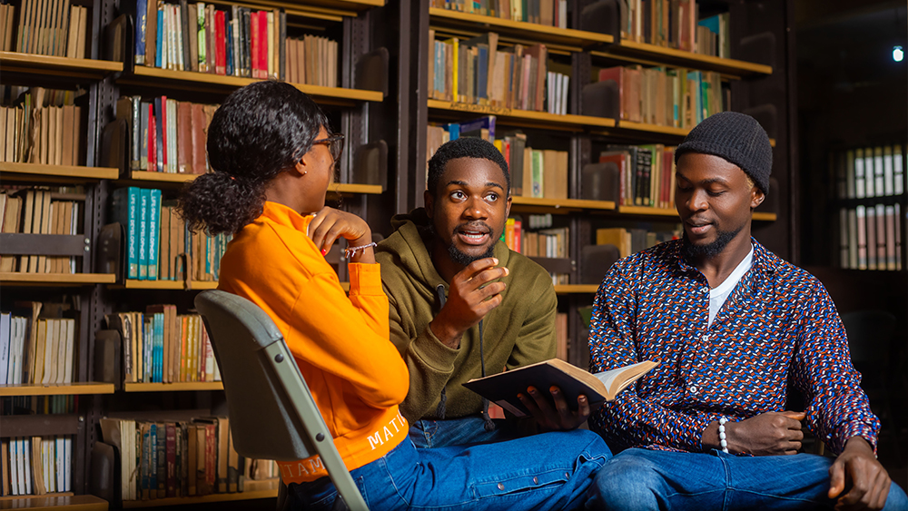 Three international students from Nigeria sit in the library at their US university and discuss their latest assignment.