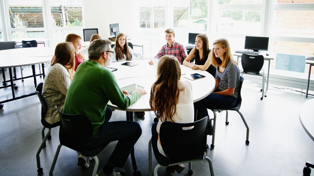 A group of university students and a professor sit around a table during a general education class at a US university