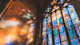 This image shows an oversized stained glass window at a Christian college in the US reflecting colorful sunbeams on an adjacent stone wall.