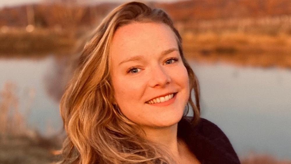 Katelyn Hill, student services advisor and professor at American Collegiate, DC, stands in front of a pond and smiles for the camera.