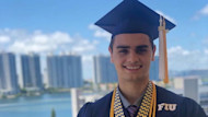 Joao, an FIU international student from Brazil, stands on a waterfront balcony in his graduation cap and gown