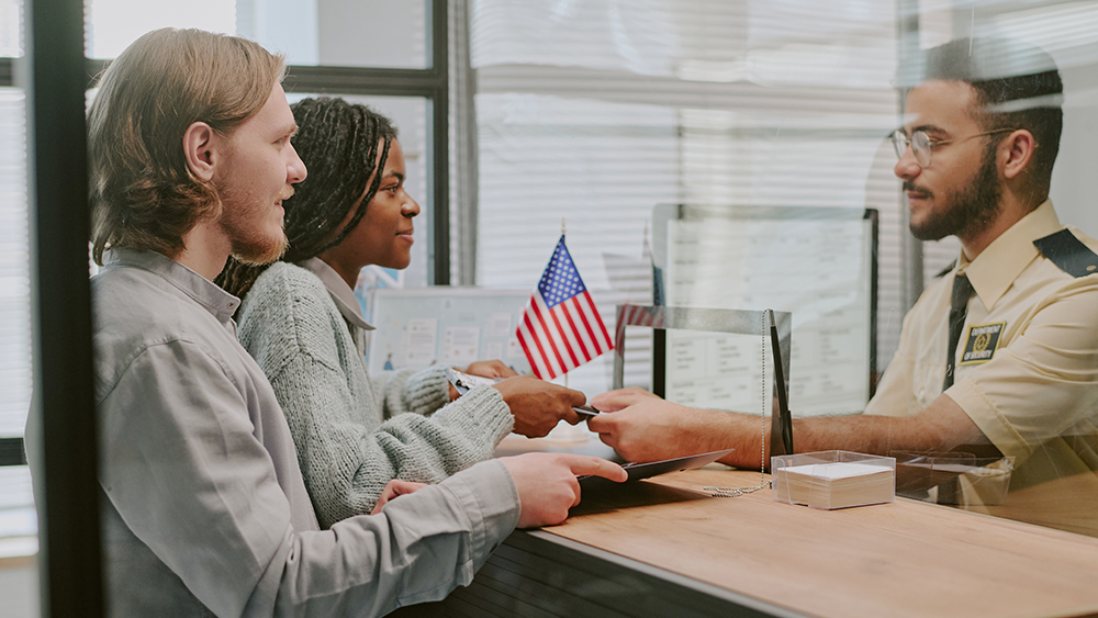 Two international students stand at the immigration and customs enforcement office desk after arriving in the US and present their SEVIS data so they can head to their university.