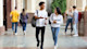 A male and female student with backpacks and carrying notebooks and walking while having an animated discussion.
