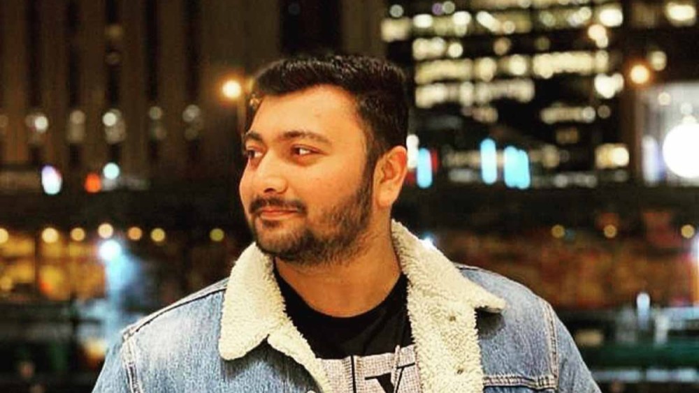 Avadh, a UIC international student from India, stands in front of a bar wearing a denim jacket with his hands in his pockets