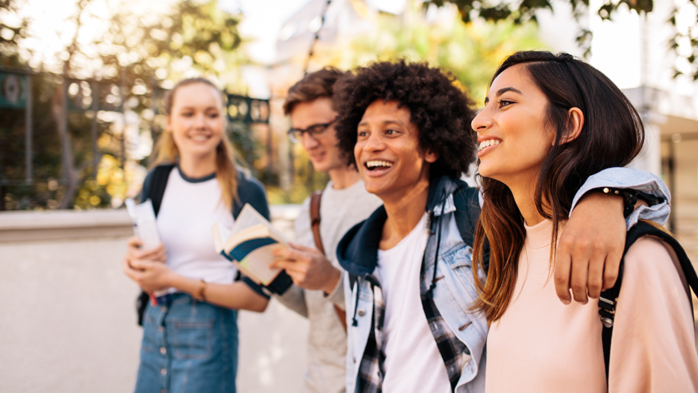 Four international students studying in the USA walk outside on their university campus 