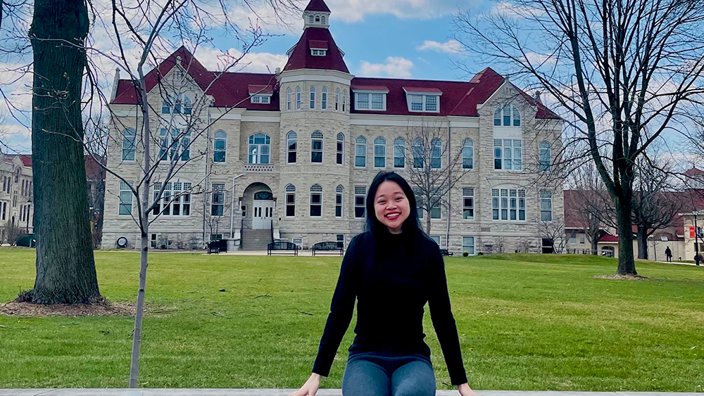 Ivy, an MBA candidate and international student from Vietnam, sits on a stone wall on the Carroll University campus.