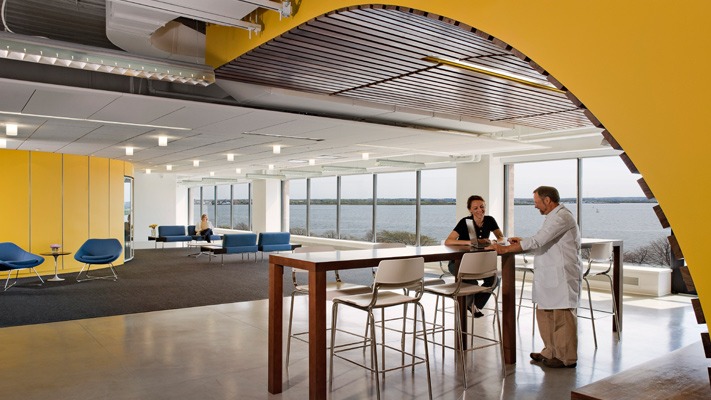 A female international student sits at a table at the University of Massachusetts Boston Venture Development Center startup incubator and speaks to a professor in a lab coat