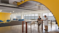 A female international student sits at a table at the University of Massachusetts Boston Venture Development Center startup incubator and speaks to a professor in a lab coat