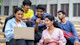 A group of international students from Bangladesh sit outside at their US university and work on a group project together on one laptop.