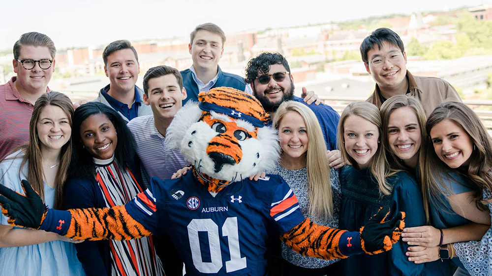 A group of international students at Auburn University stand behind Aubie the Tiger, the Auburn University school mascot.