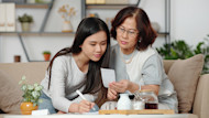 A female international student from Asia and her mother sit on a sofa and look at paperwork going over budgeting for the costs of studying in the US.