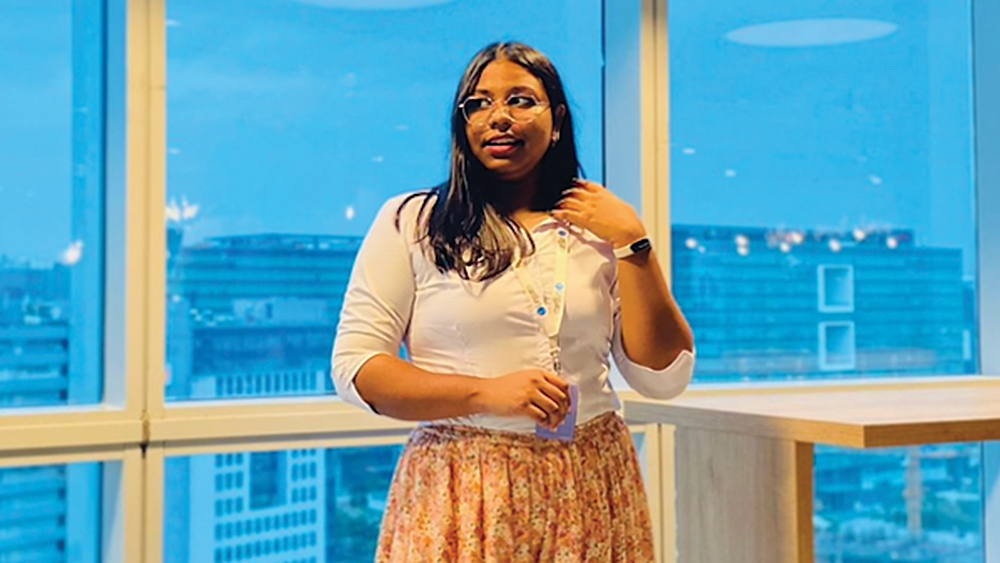 Nandini, an international student from India studying at The University of Texas at San Antonio, stands in front of a wall of windows and looks off camera. 