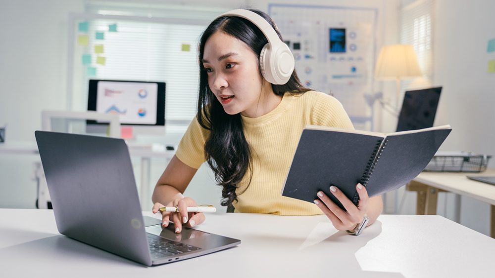 A female international student at a US university works on a laptop and wears earphones as part of her digital classroom learning experience.