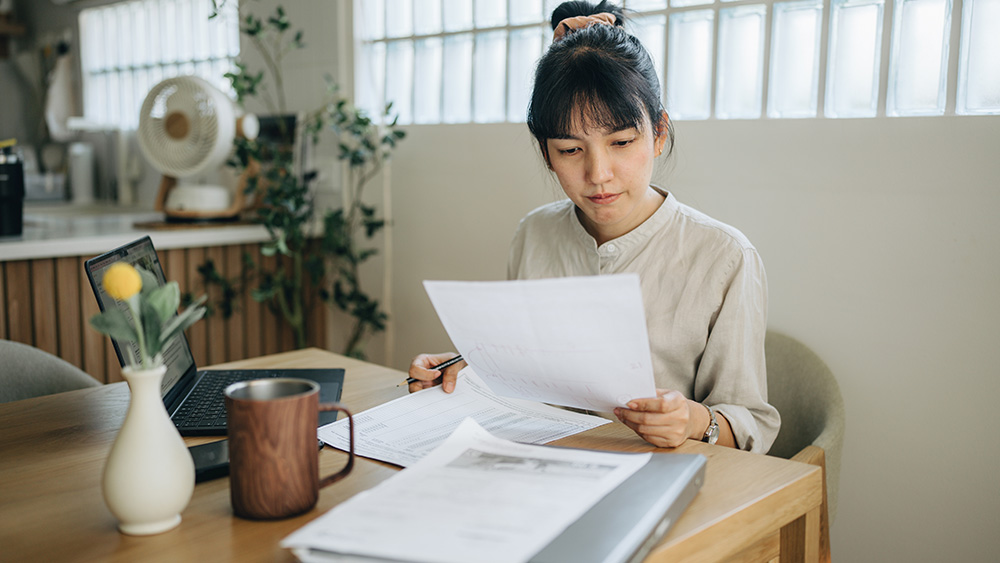 A female international student from Asia reviews her student visa paperwork before checking the status of her F-1 visa to travel to the US and attend her US university.