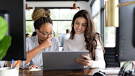 Two female international students sit side by side in front of a laptop