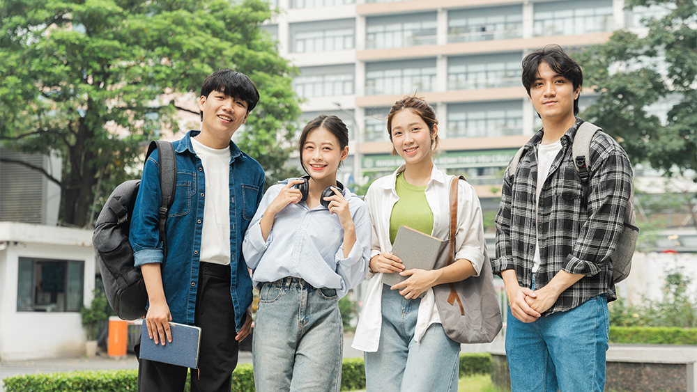 Four Chinese international students stand side by side at their US university campus before heading to class. 