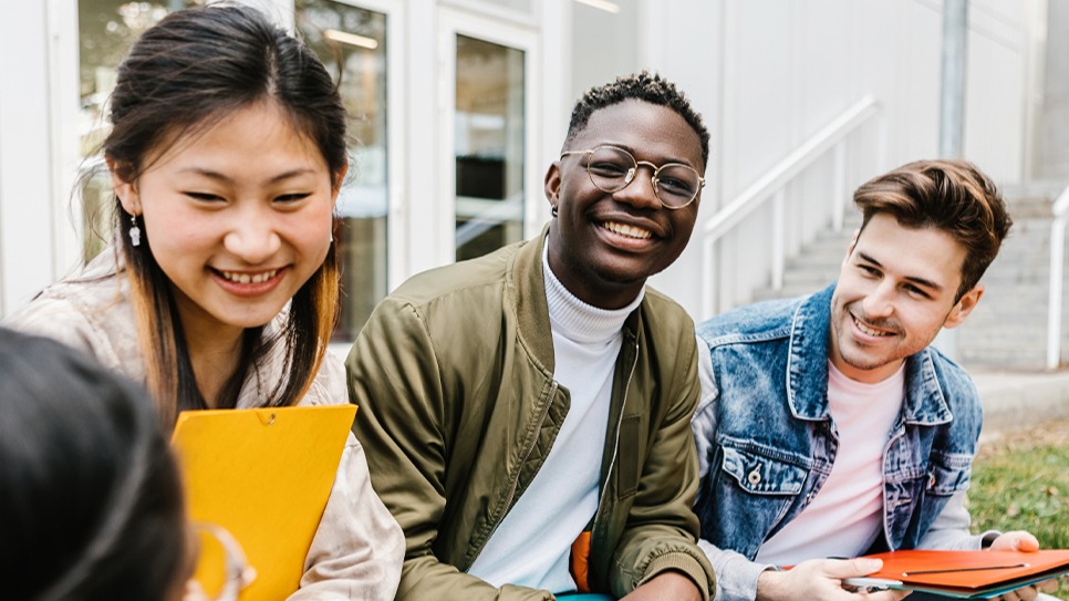 Three international students with the Applied AI in Engineering Summer Institute at the University of California, Berkeley, in collaboration with Shorelight, sit together on campus and laugh during a break. 