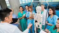 International nursing and medical students studying at medical colleges in the US stand in scrubs while being taught on site at a local hospital near their university.