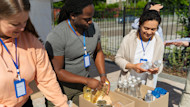 Three volunteers stand in a row outside a water donation table in New Orleans and count water bottles
