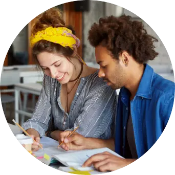 Two individuals sit at a table, working together in a workbook on the table.