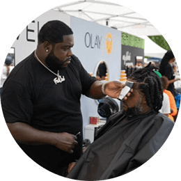 Black consumers experience innovative brands at My Black Is Beautiful, Olay and Bevel stations during the HBCYOU Tour. In the inset, a Black man is seated in a chair and receives a haircut from a barber.