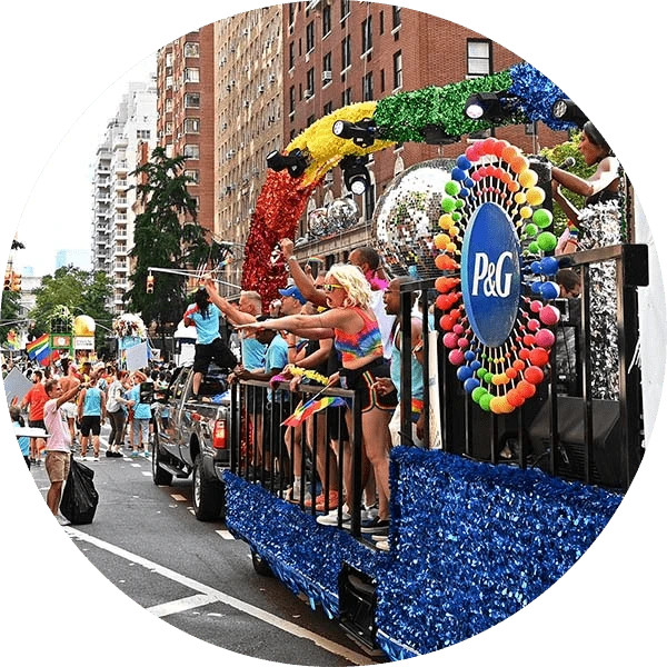 Several people stand on top of a rainbow-colored parade float at a Pride parade.