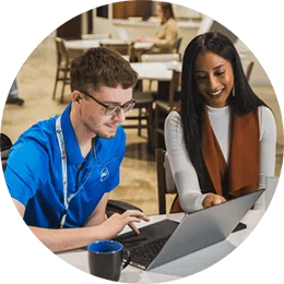 Two P&G employees sitting at a desk smiling and looking at a laptop in one of P&G's meeting spaces.