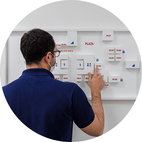 A man in a dark blue shirt faces and points at a white board with several white 3D models on it.