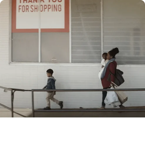Screenshot from Widen the Screen movie. Woman walking and holding her child in her arms. Her second child walking in front of her.