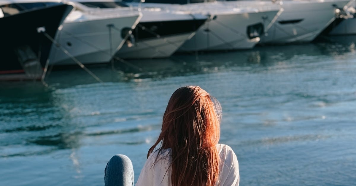 A woman sitting on the edge of a dock looking at boats