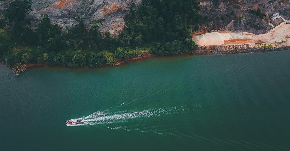 Drone view of boat floating on water surface of turquoise ocean near green coast with trees and rocks