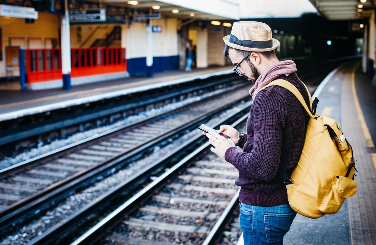 man-standing-on-train-station-platform-with-phone-in-his-hands-211052