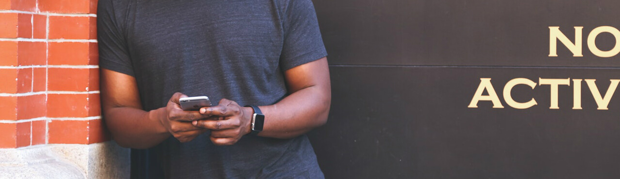 man holding phone in hands leaning against the wall