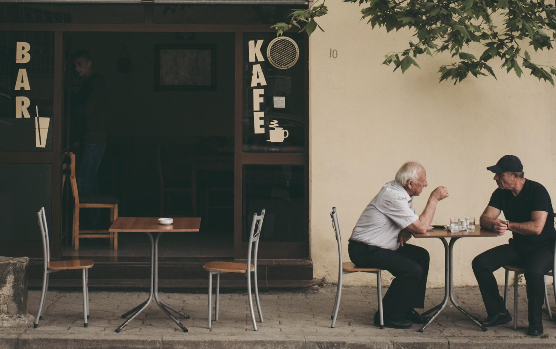 two elderly men talking outside of cafe
