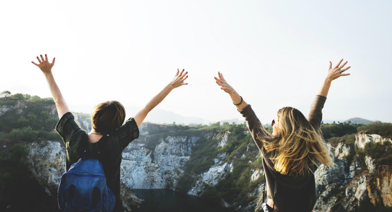 two friends with hands in air on top of mountain