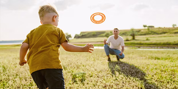 Vater und Sohn, die im Sommer in der Wiese Frisbee spielen