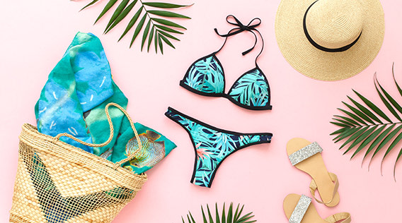 Bikini, Sonnenhut, Strandtasche und Palmblätter flatlay auf rosafarbenem Hintergrund