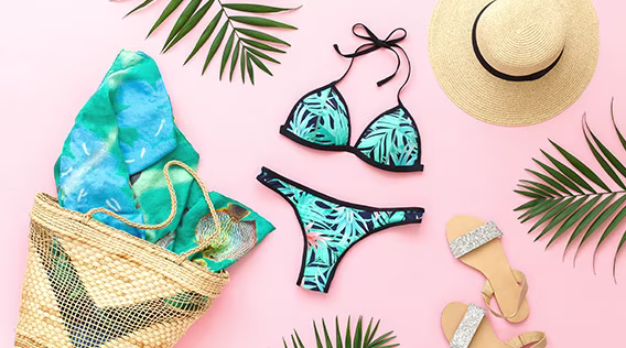 Bikini, Sonnenhut, Strandtasche und Palmblätter flatlay auf rosafarbenem Hintergrund