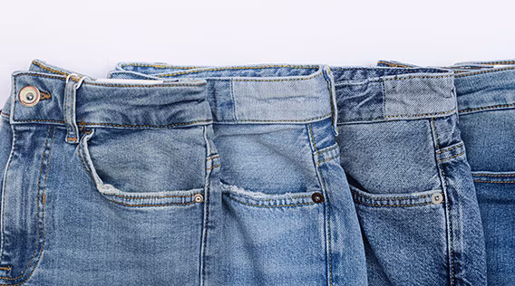 Vier blaue Jeanshosen die aufgereiht daliegen