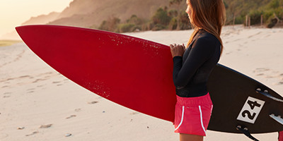 Eine Frau steht am Strand mit einem Surfboard.