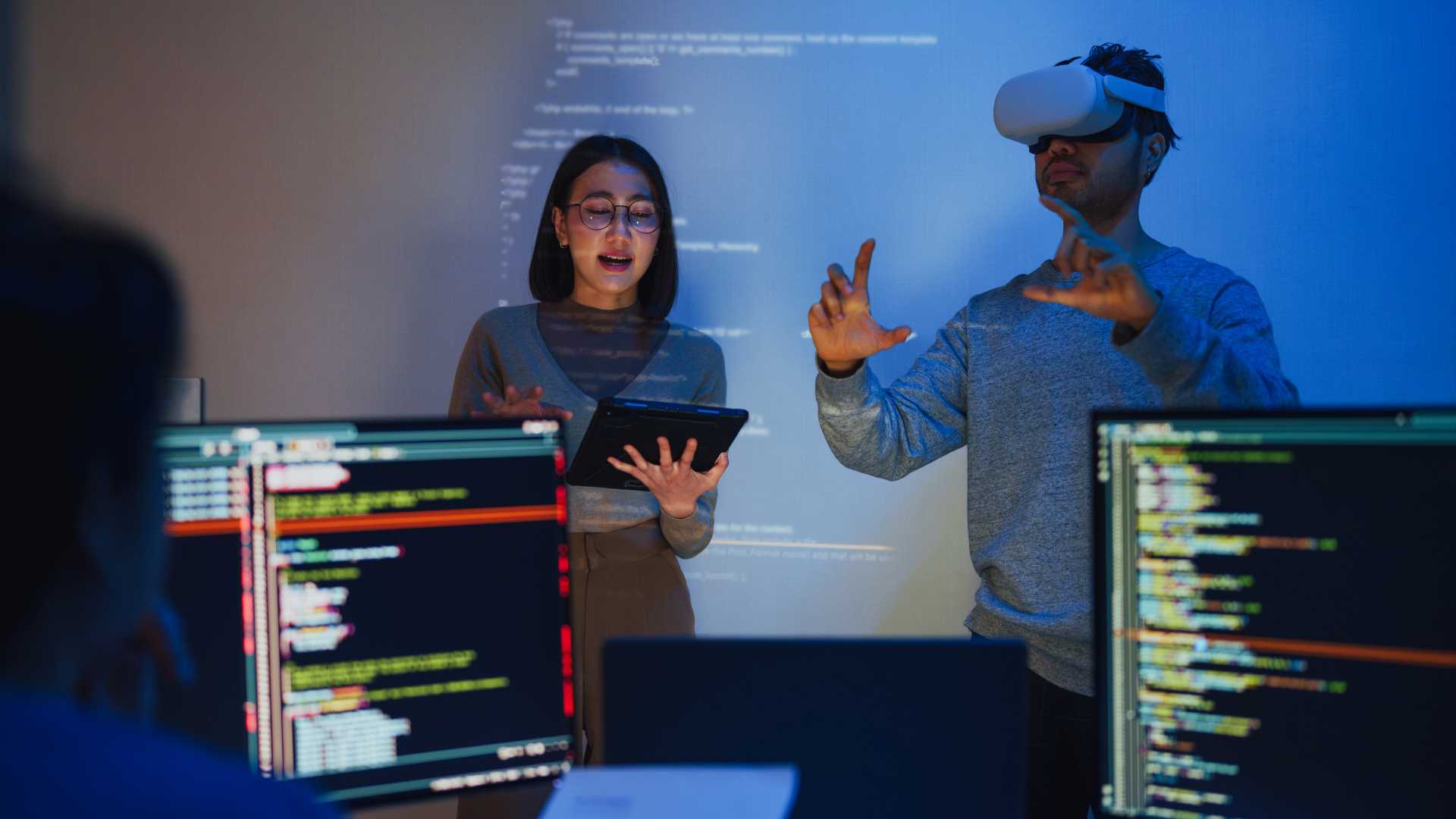 Two colleagues running an immersive simulation session, one wearing a VR headset and one reviewing results on a tablet, representing technology-led practice that scales beyond manager availability.