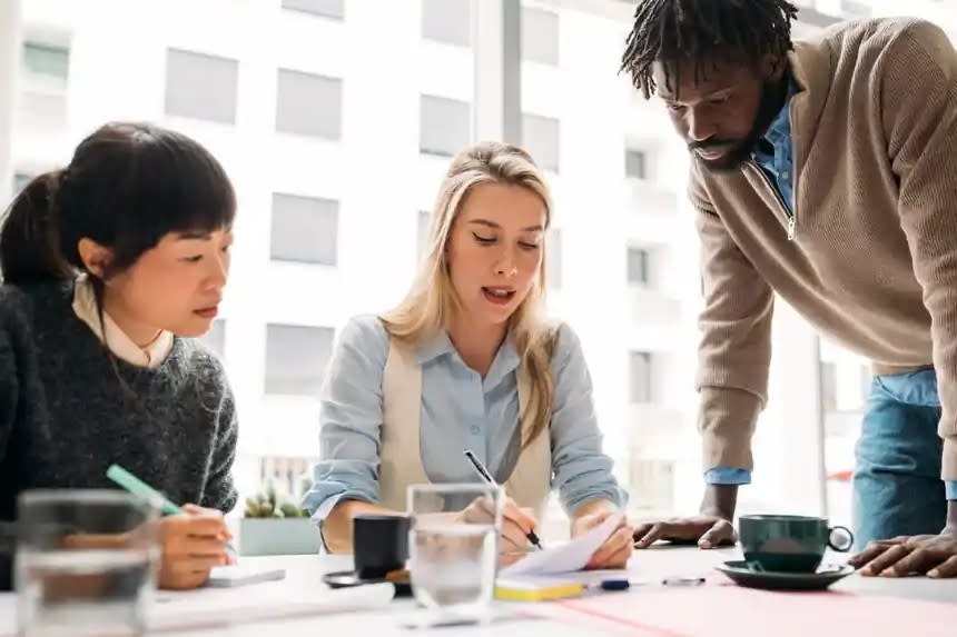 Three sales enablement colleagues reviewing cohort training data and skill scorecards together during a working session