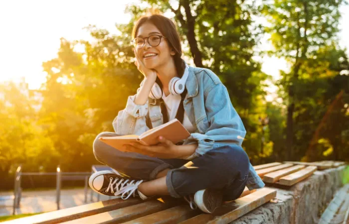 Jeune fille souriante assise sur un banc et lisant un livre
