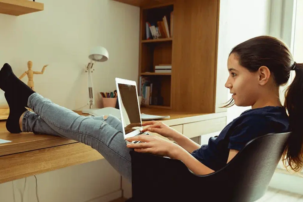 Jeune fille assise à son bureau avec ordinateur portable